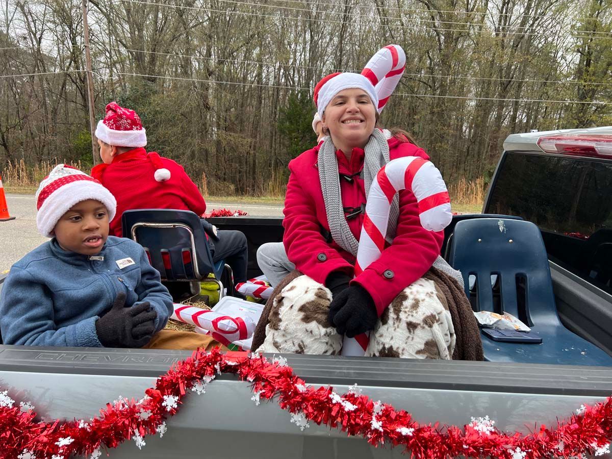 People in Santa hats riding in a decorated truck with a dog during a holiday event