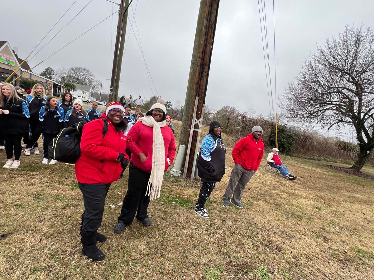 People in winter coats standing on a grassy field near a utility pole, with a group in the background