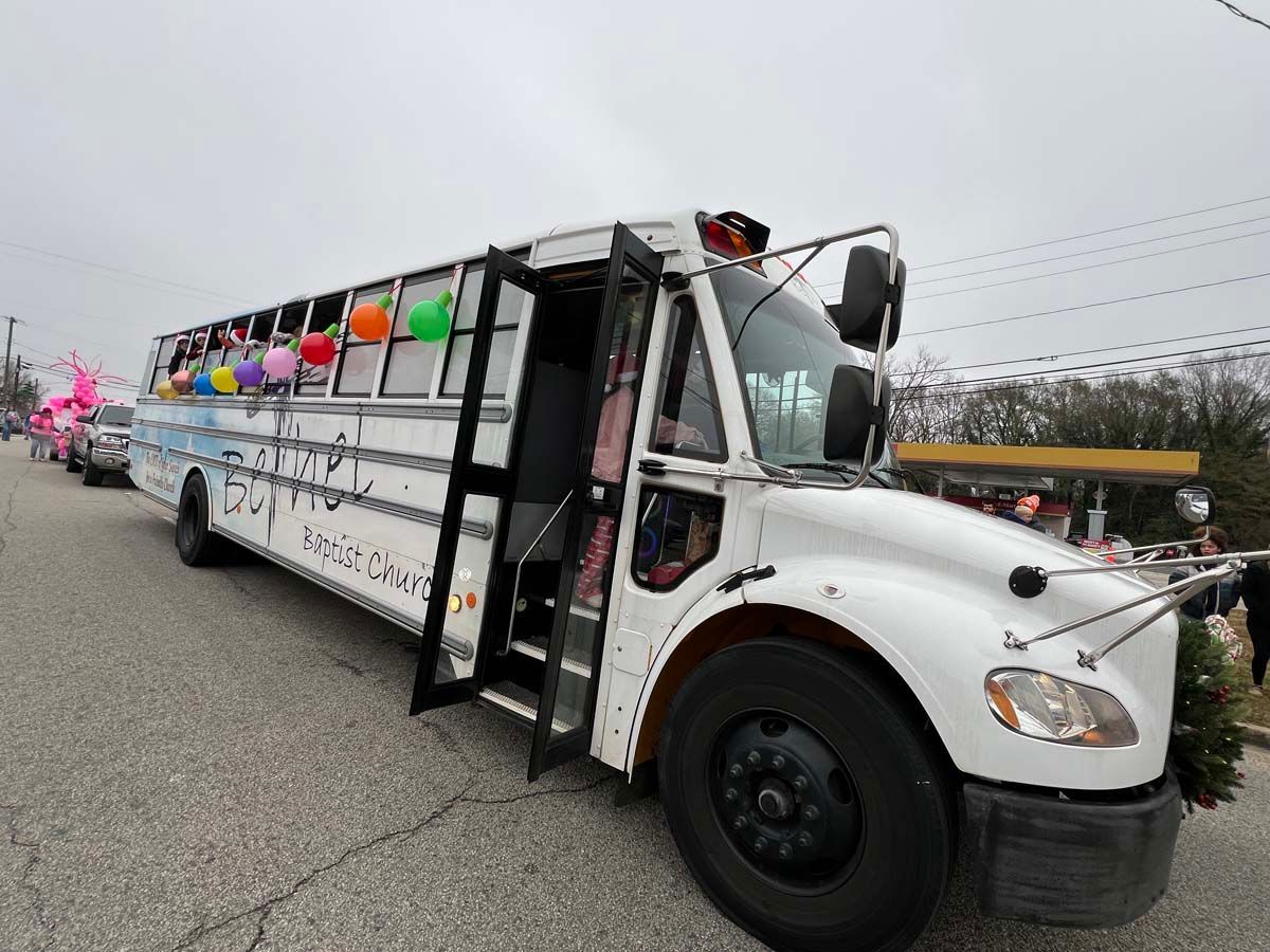 White shuttle bus with open door and colorful seats driving on a road under an overcast sky