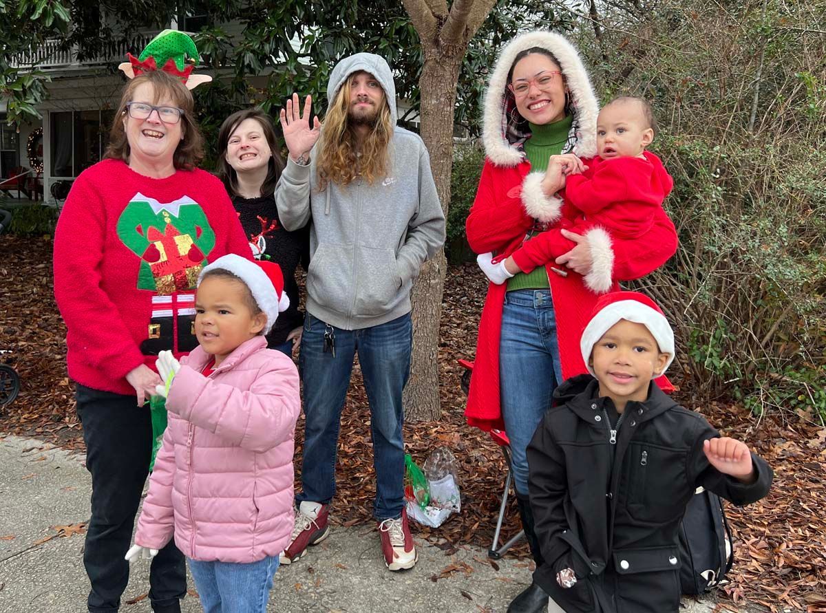 Family in festive red and green holiday outfits posing outdoors by a tree