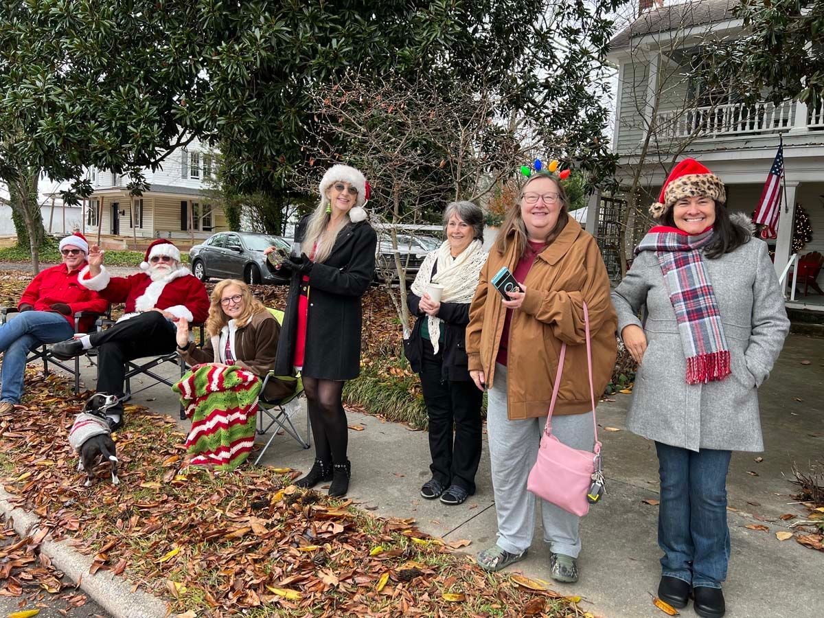 People in holiday costumes posing on a sidewalk with a decorated house in the background