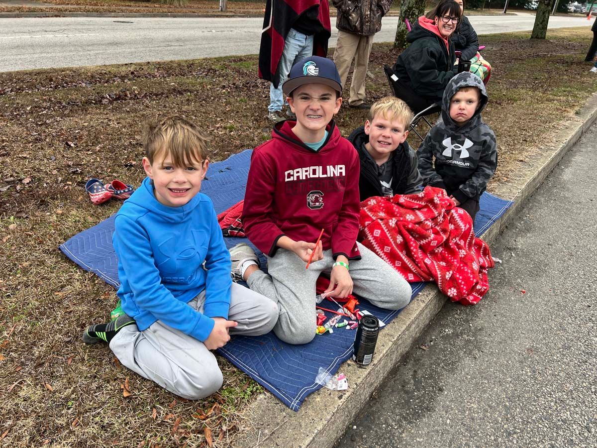 Children sitting on a blanket outdoors, smiling and wrapped in red blankets on a chilly day