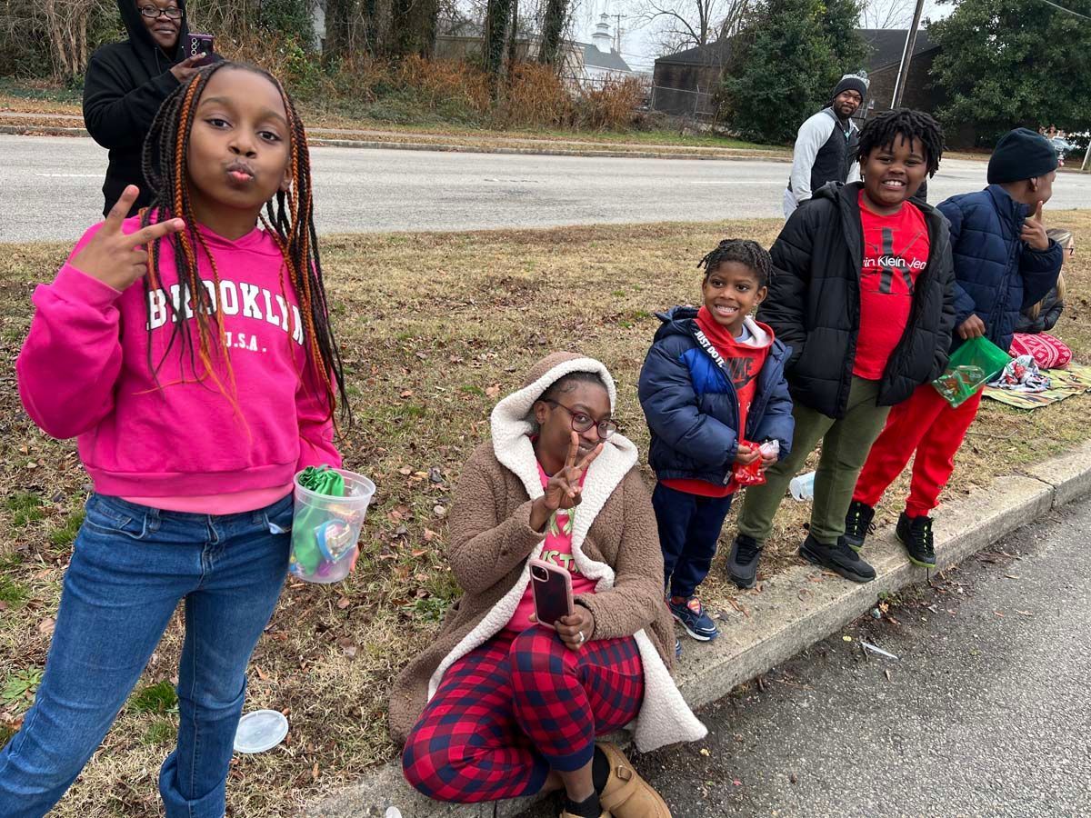 Five children standing and sitting on a roadside, posing outdoors in colorful winter clothes