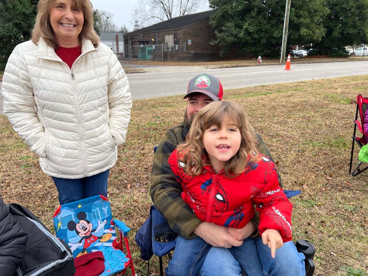 Woman standing beside child seated on lap outdoors, with decorated bag and road in background