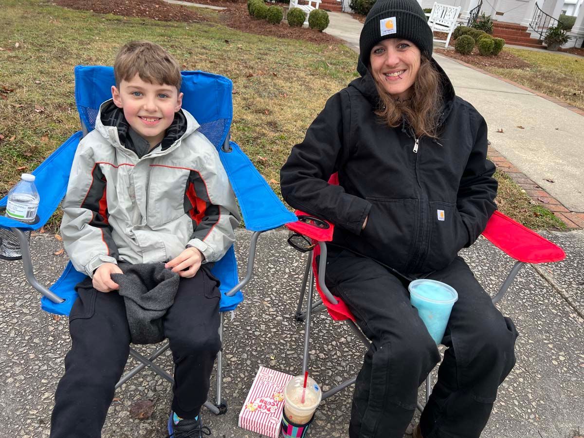 Two people sitting in folding chairs on a driveway, smiling with drinks beside them.