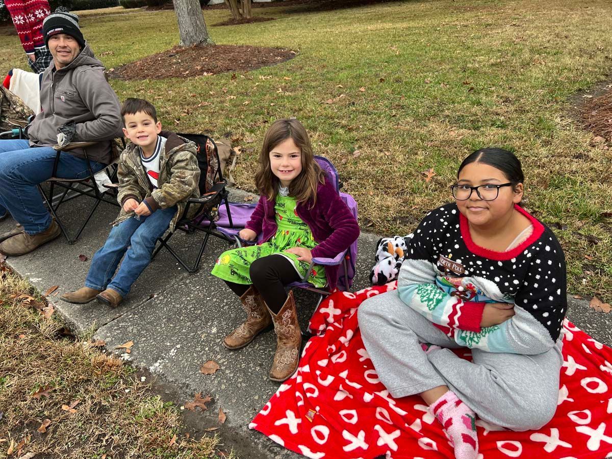 Four people sitting on a curb outdoors with blankets and gear in a park-like setting