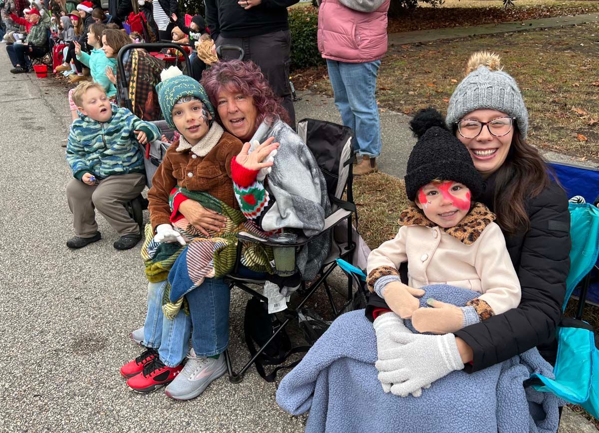 People seated outdoors in winter clothes, smiling and posing at a crowded event with a child on each lap