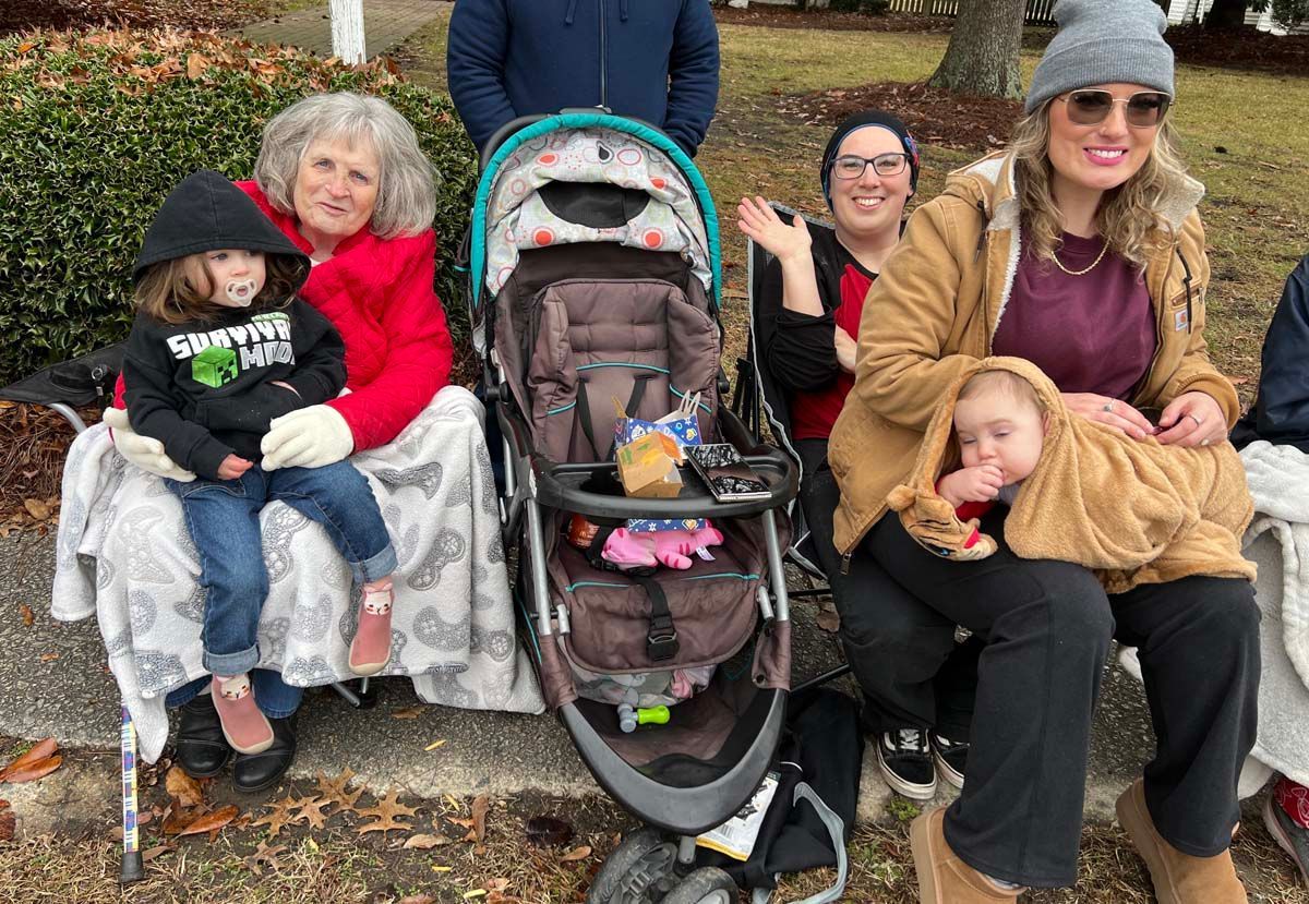 Group sitting outdoors in autumn, with a stroller in the center and one person waving
