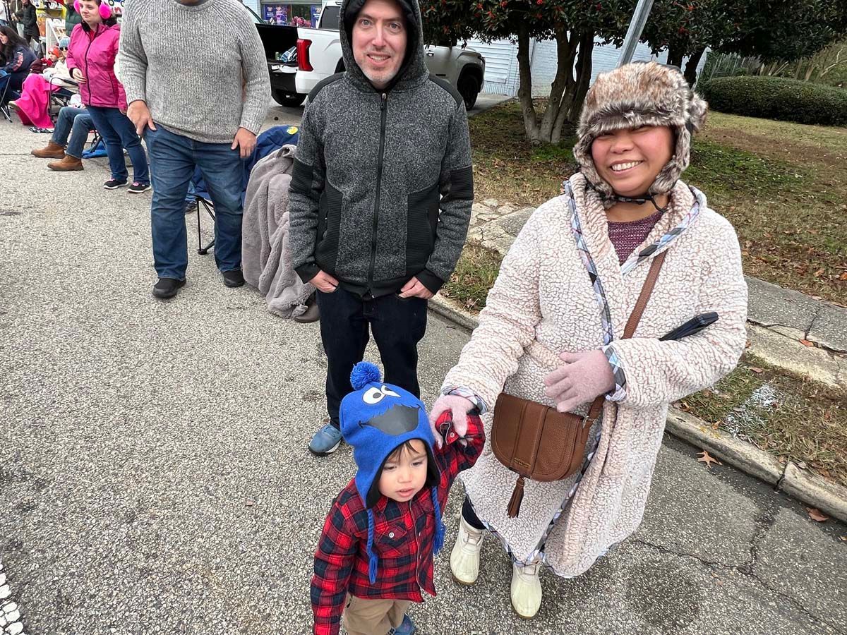 People in winter coats stand with a child in a blue hat on a park path.