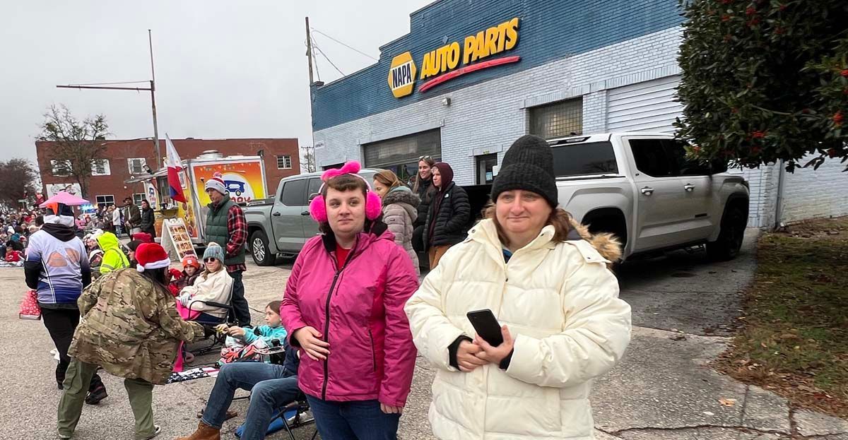People waiting in a line outside a pawn shop on a cloudy day, with two women in bright jackets in front.