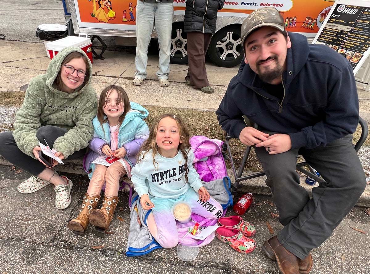 Family posing outdoors with three children, holding Easter baskets and eggs beside a decorated vehicle.