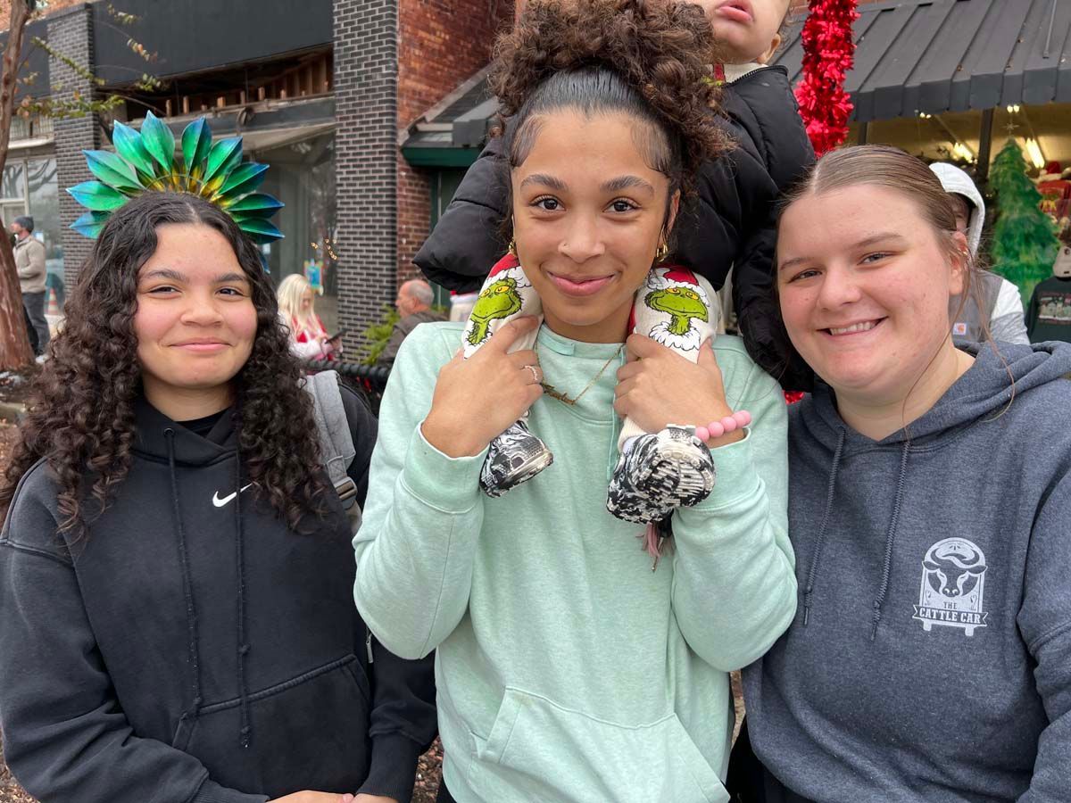 Three people smiling outdoors, holding decorated items and wearing casual hoodies.