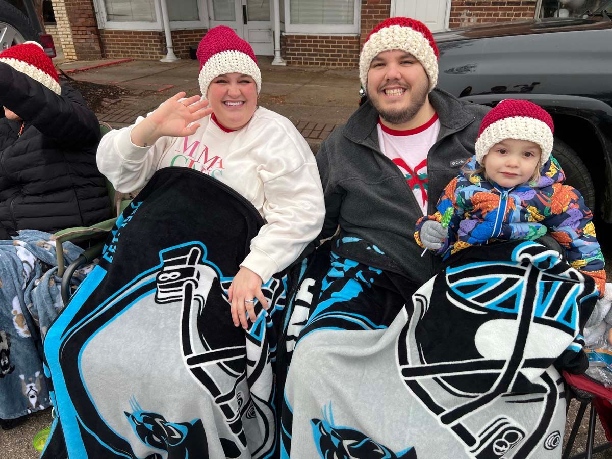 Four people in Santa hats sit on decorated motorcycles, smiling and waving outdoors.