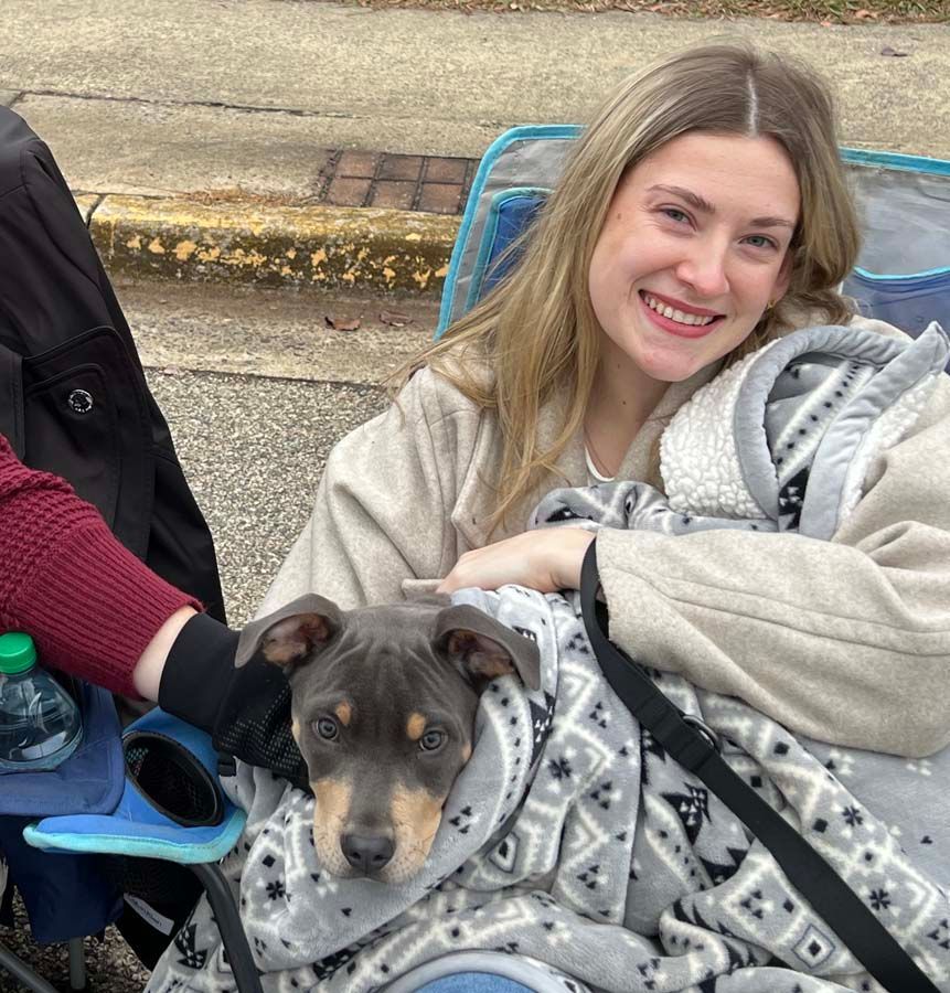 Smiling person holding a small dog wrapped in a patterned blanket outdoors