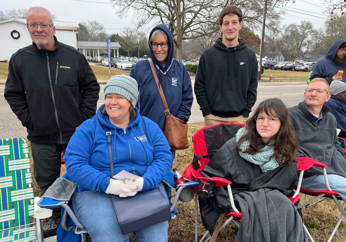 Group of people outdoors on a chilly day, some seated in chairs and others standing nearby.