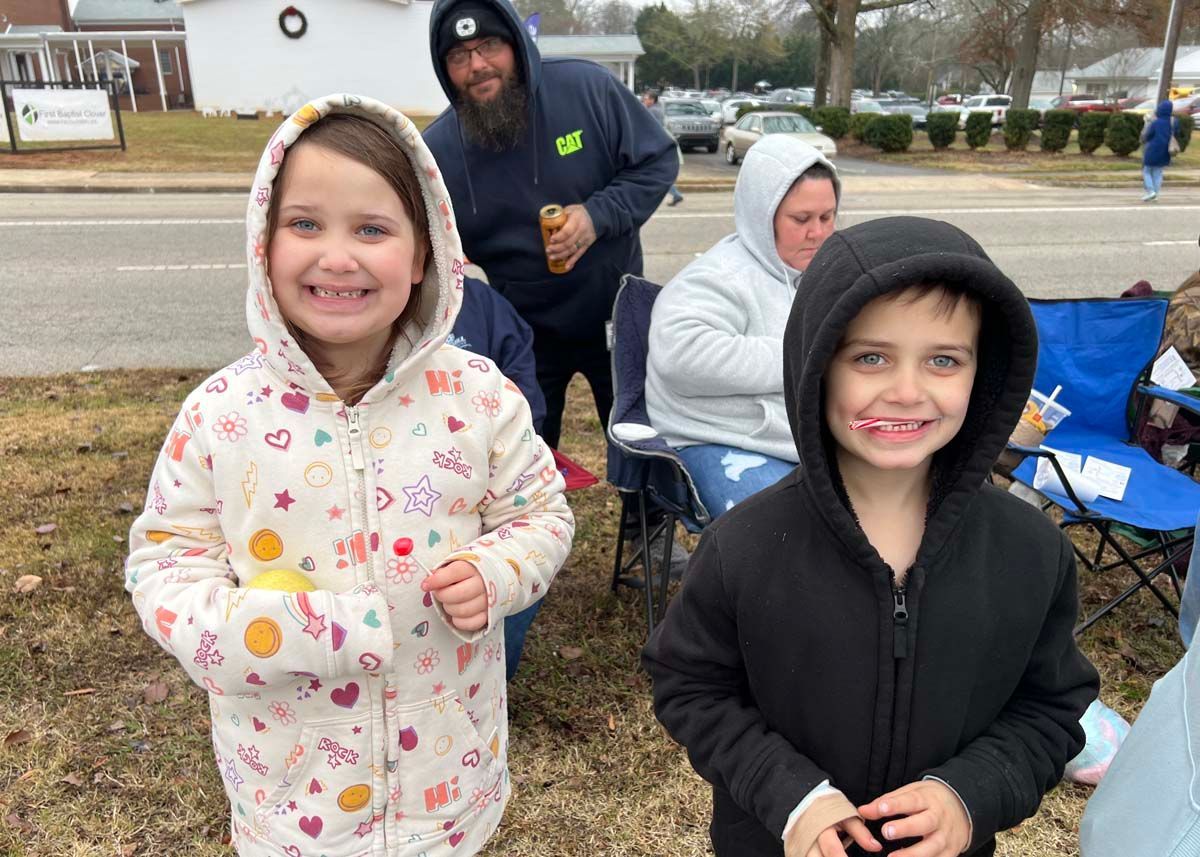 Children in winter coats smiling outdoors at a roadside gathering