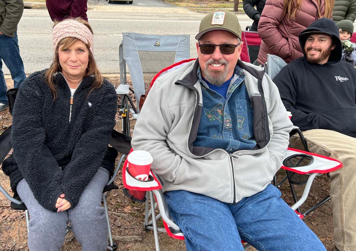 Three people sitting in folding chairs outdoors, smiling at the camera.