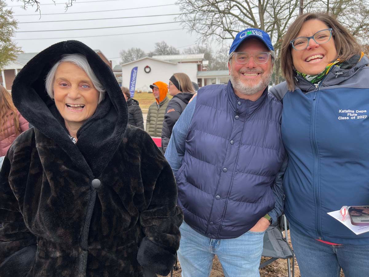 Three smiling people in winter coats standing outdoors on a cold day.