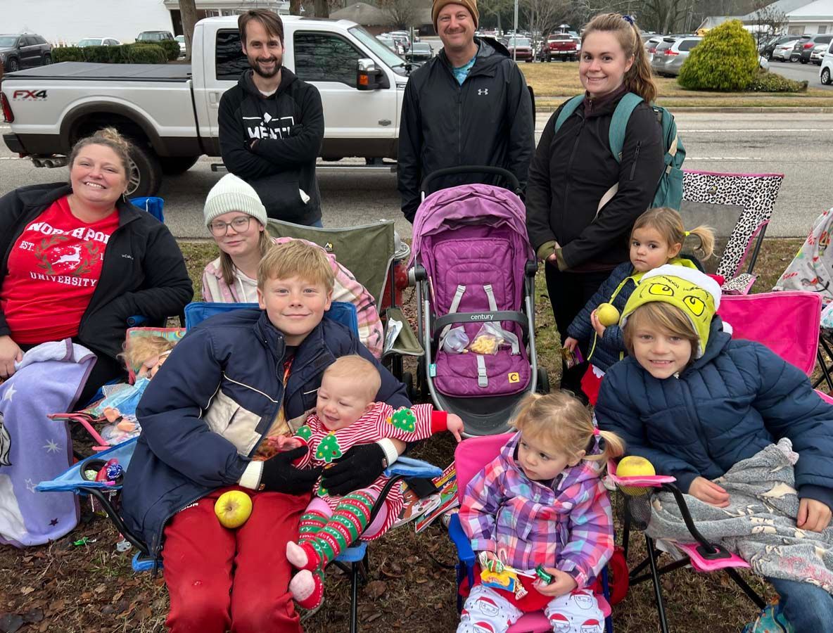 Group of people posing outdoors with strollers and children in colorful coats by a road
