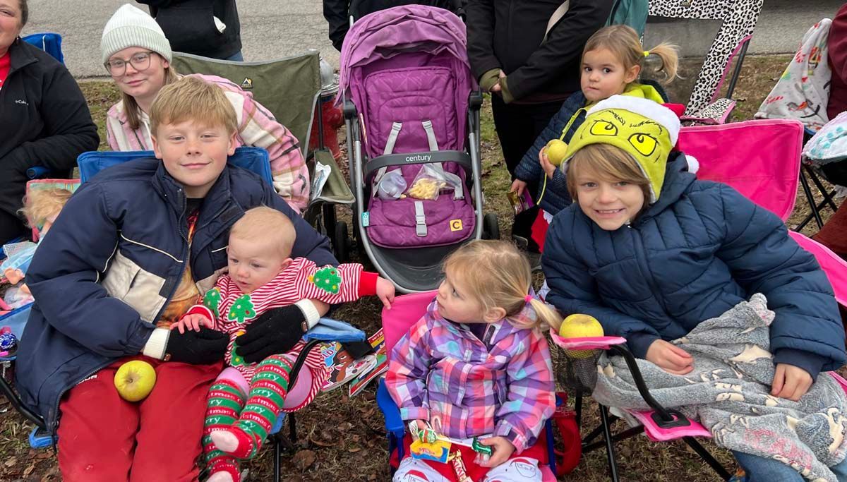 Children sitting on blankets outdoors, bundled in winter hats and jackets, with strollers behind them