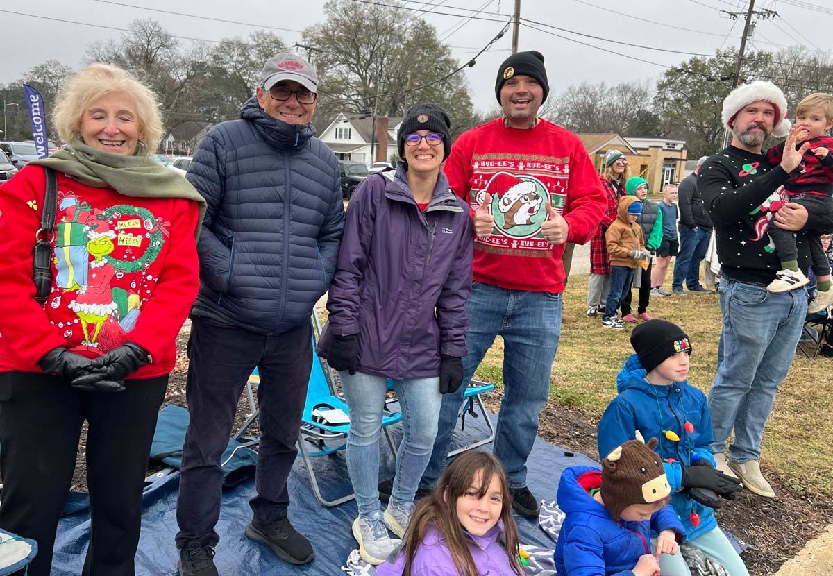 People in winter clothes standing outdoors with children sitting in front of them.