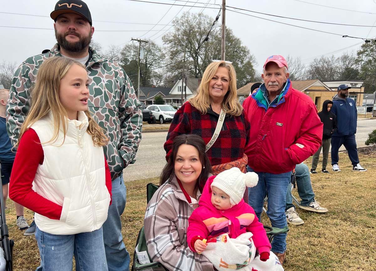 Family group standing outdoors on a cloudy day, with adults and two children in winter jackets.