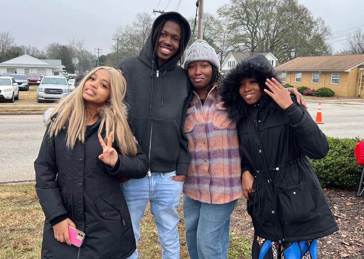 Four friends posing outdoors on a cloudy day, smiling and making peace signs.