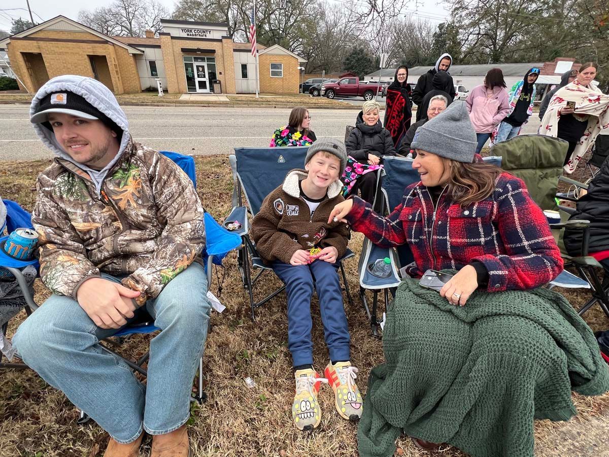 People sitting on a bench outdoors, smiling and talking in a park on a chilly day.