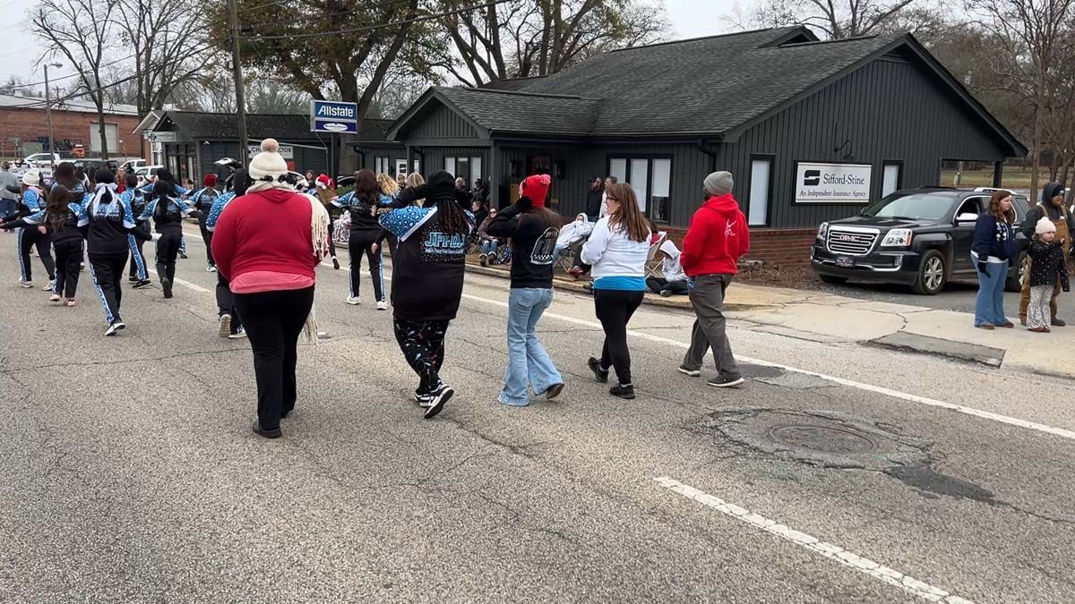 People walking across a street toward a dark building on an overcast day.