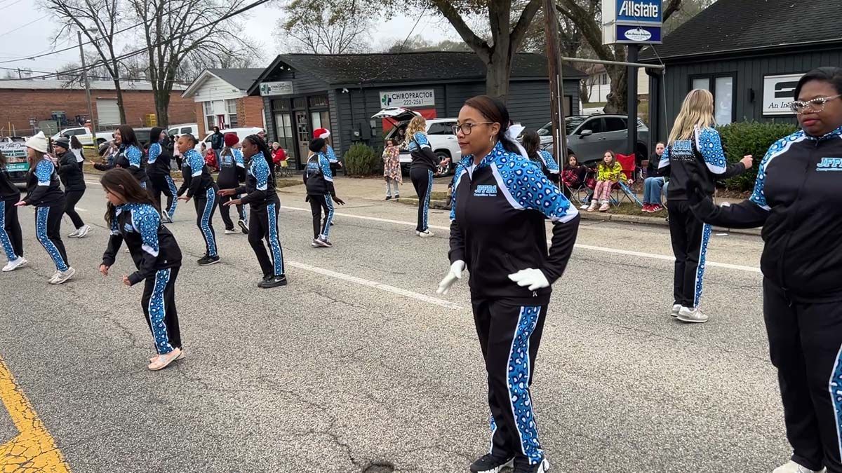 People in matching tracksuits perform a synchronized dance on a street during an outdoor event.
