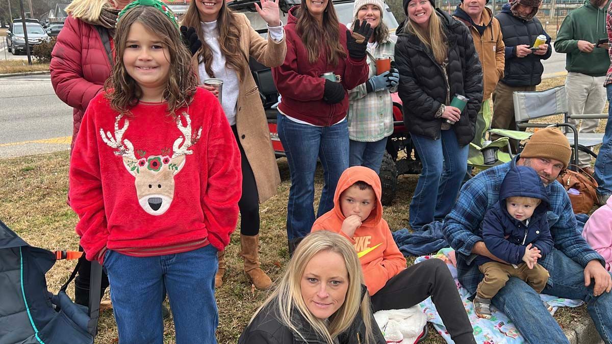 Group of people outdoors in winter, wearing coats and a red reindeer sweater, posing together.