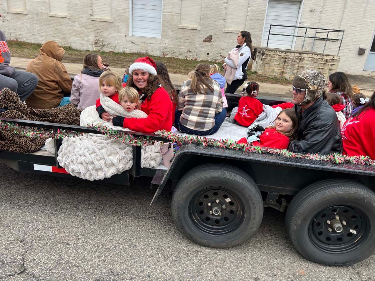 People seated in a decorated trailer, one wearing a Santa hat, during a holiday parade.