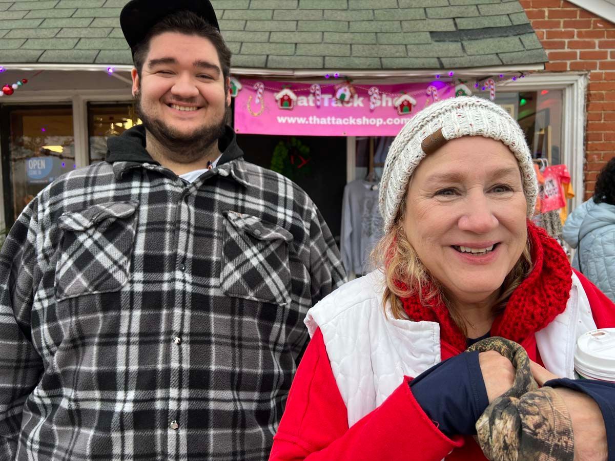 Two people smiling outdoors in winter clothes in front of a pink storefront