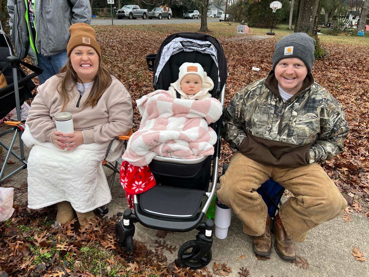 Three people sit outdoors on a bench and stroller, bundled in coats and blankets on a chilly day.
