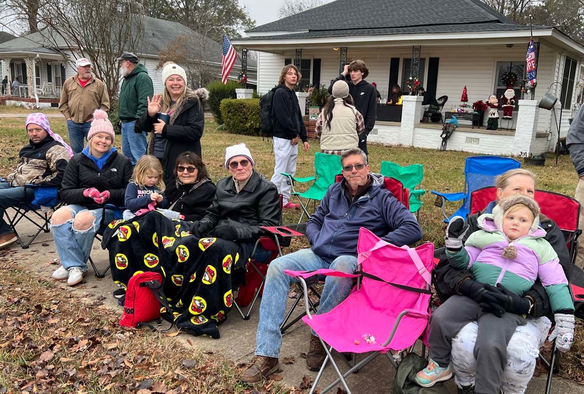 People seated in folding chairs outdoors at a neighborhood gathering in front of a house.