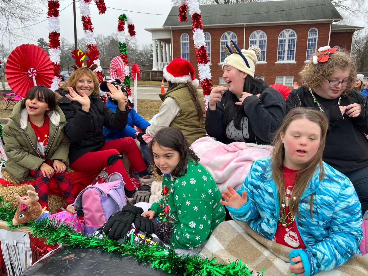 People sitting on a parade float, wearing festive red and green holiday outfits.