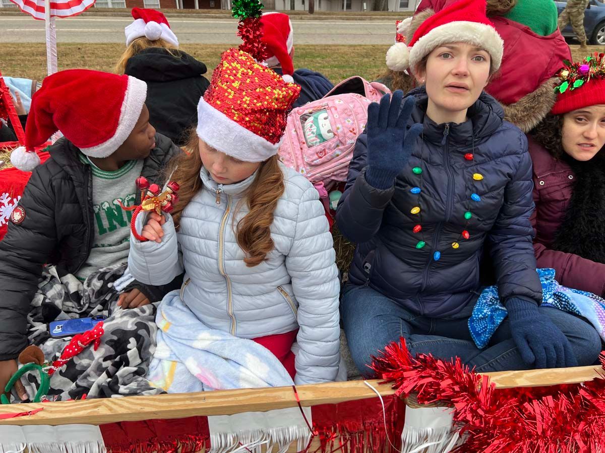 Children in Santa hats sit on a decorated float, smiling and bundled in winter coats.