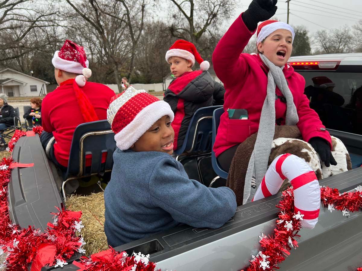 Children in Santa hats riding in a decorated parade wagon, waving and smiling