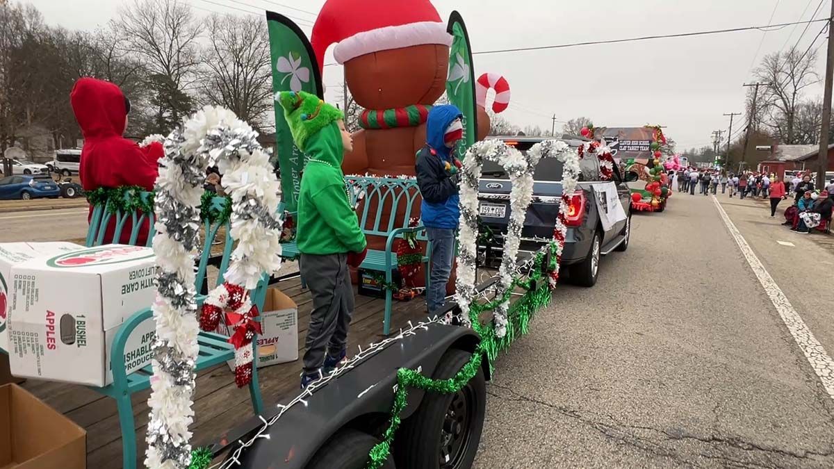 Holiday parade floats lined with people in festive costumes and Christmas decorations along a road
