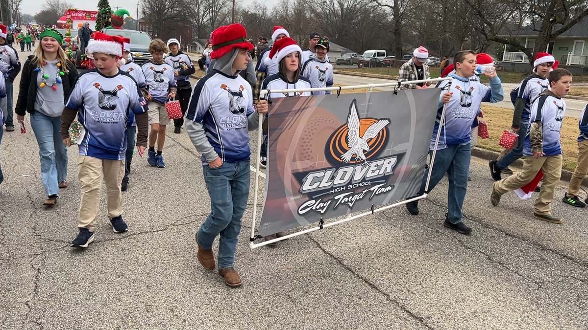 People in Santa hats march behind a Clover banner in a winter parade.
