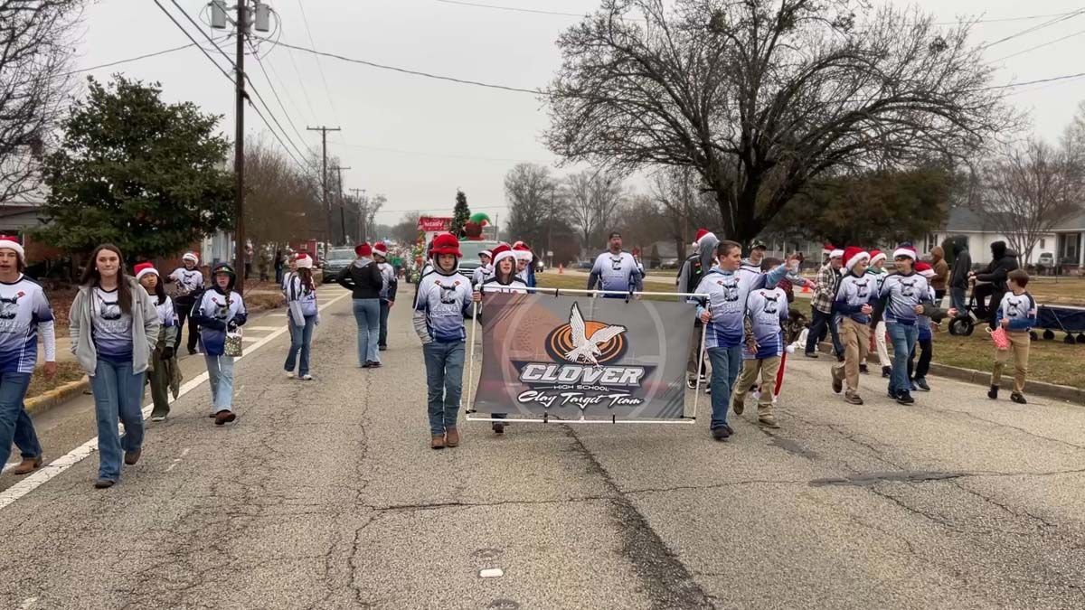 Football players marching in a parade, holding a team banner on a cloudy street.
