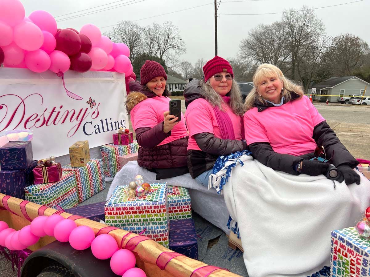 Three people in pink sit on a pink-decorated parade float with a “Destiny’s Calling” sign.