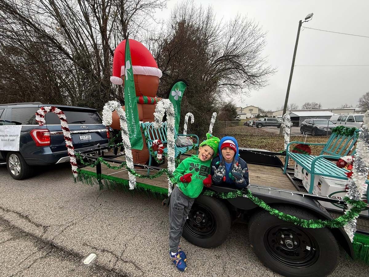 Two children sitting on a festive Christmas parade float with a Santa hat and candy cane decorations