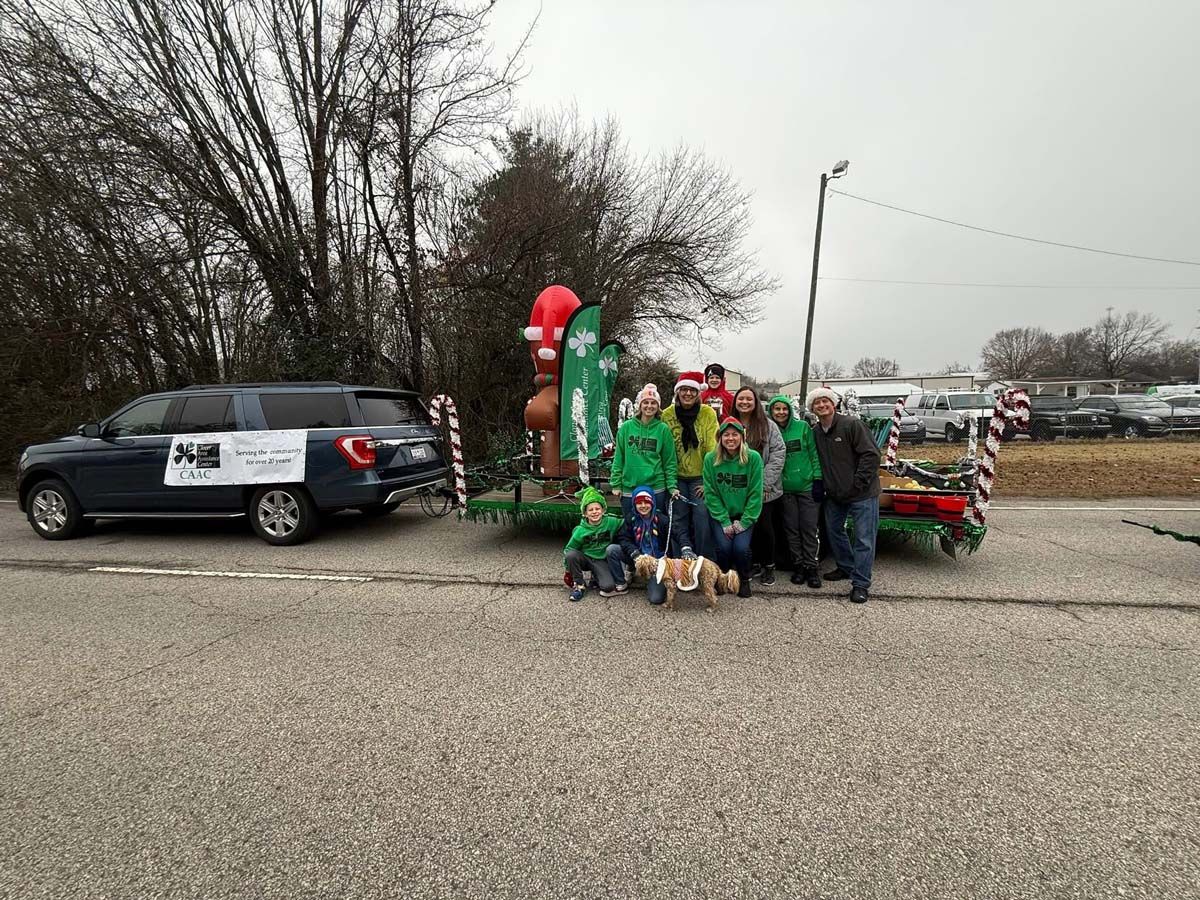 Group in green shirts posing beside a decorated car and balloon arch on a roadside