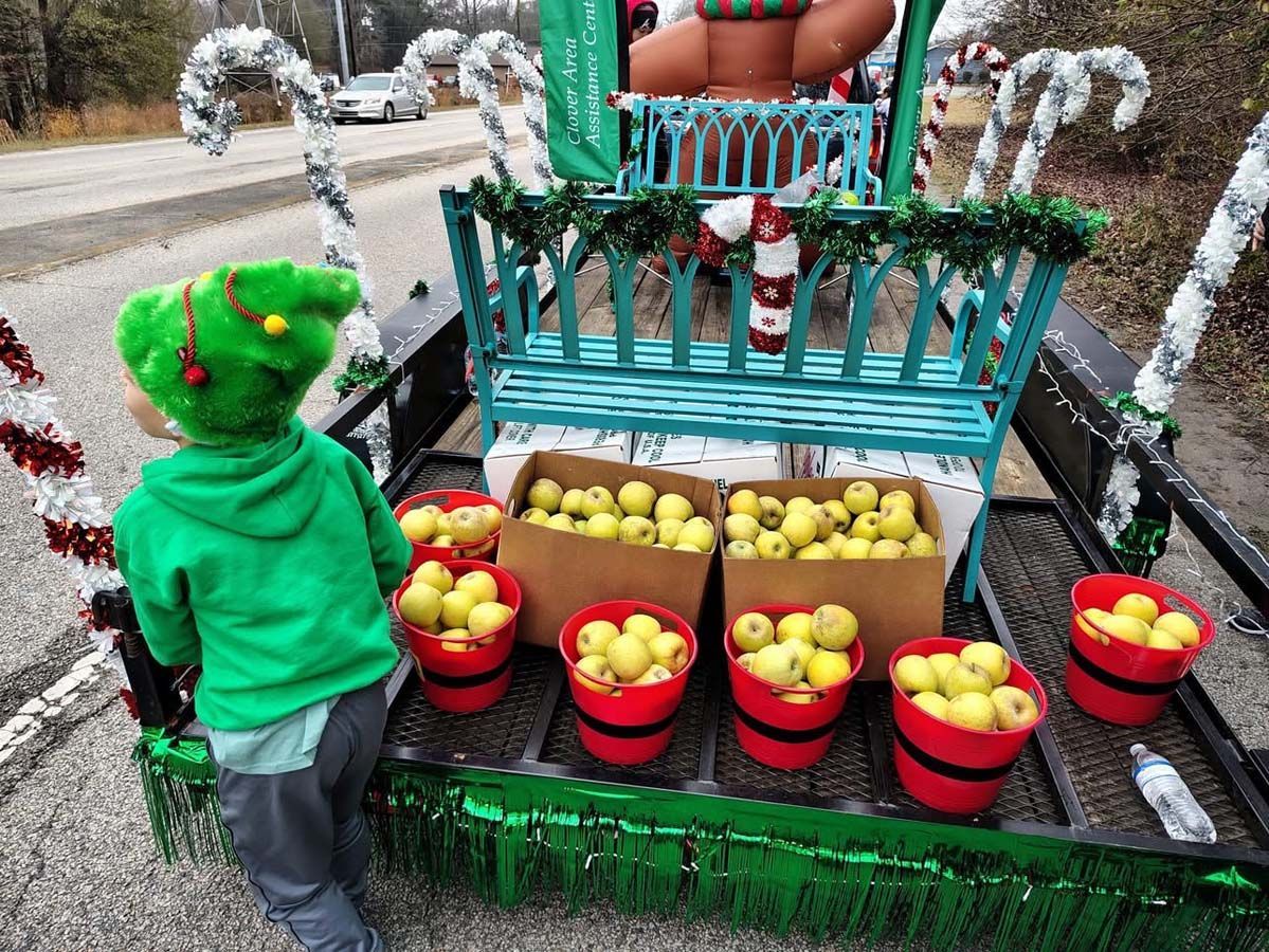 Child in green hoodie viewing apple baskets on a decorated roadside stand with candy-cane railings