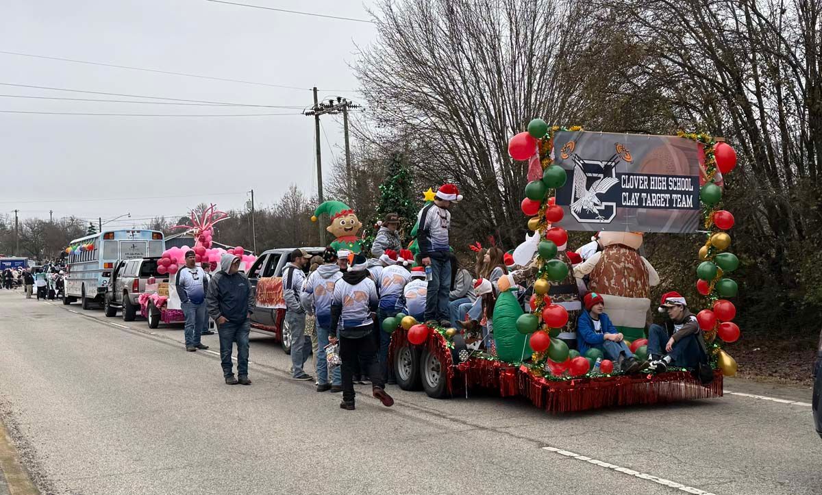 Parade float decorated with red and green balloons, people walking beside it on a roadside