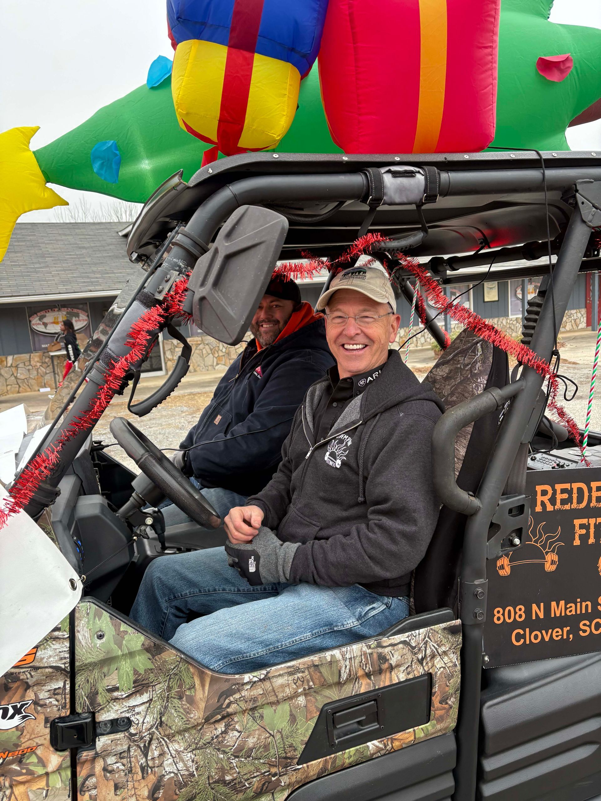 Two people smiling in an off-road vehicle with a colorful inflatable decoration overhead