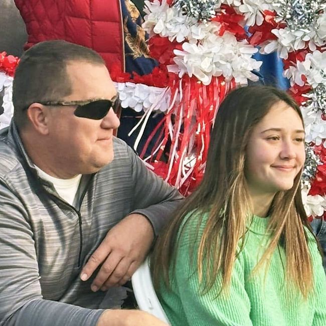 Two people sitting outdoors, smiling, with red-and-white festive decorations behind them.