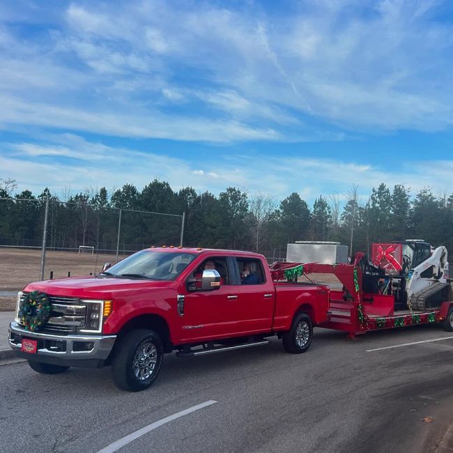 Red pickup truck hauling a red trailer with a wrecked car on a road under a blue sky
