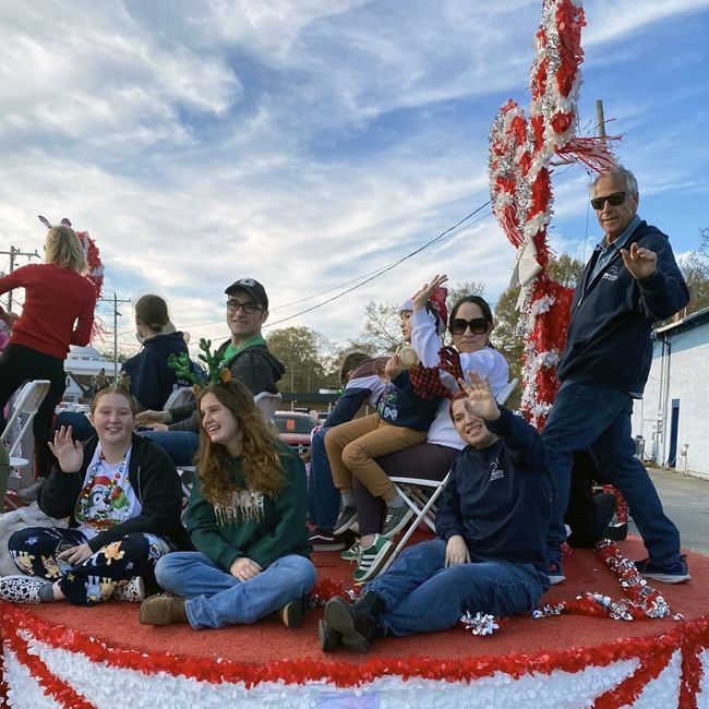 People sitting on a red float decorated with white streamers during a parade under a blue sky